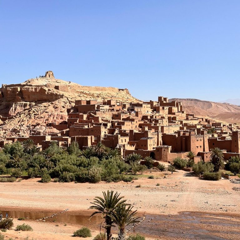 a desert town with buildings and trees with Aït Benhaddou in the background