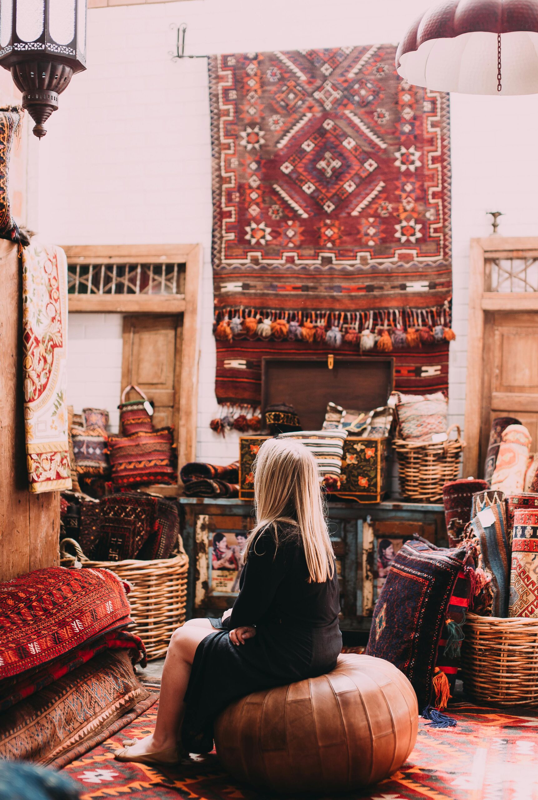 A woman sitting in a room filled with colorful Oriental carpets and woven baskets.