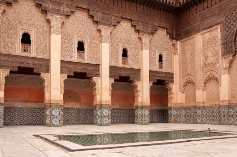 Main courtyard of ancient Ben Youssef Madrasa with arched passage and walls decorated with arabesque ornaments on sunny day in Marrakesh