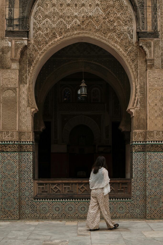 A woman walks by a beautifully decorated archway of a Moroccan mosque in Fes