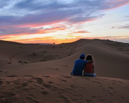 pexels-photo-12378898-12378898 A couple sitting together, embracing the stunning sunset in the Moroccan desert dunes.