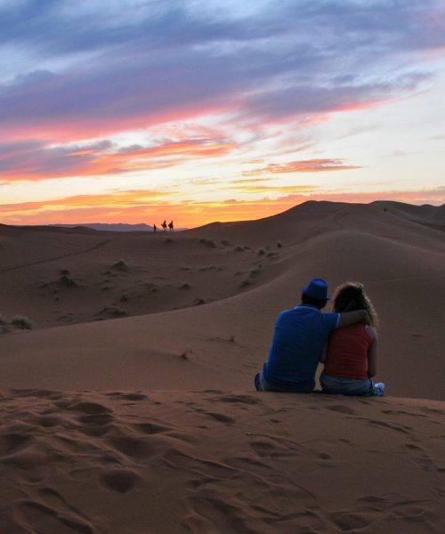 pexels-photo-12378898-12378898 A couple sitting together, embracing the stunning sunset in the Moroccan desert dunes.
