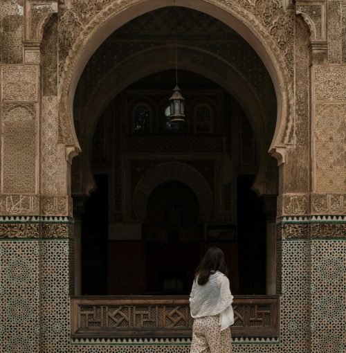 A woman walks by a beautifully decorated archway of a Moroccan mosque in Fes
