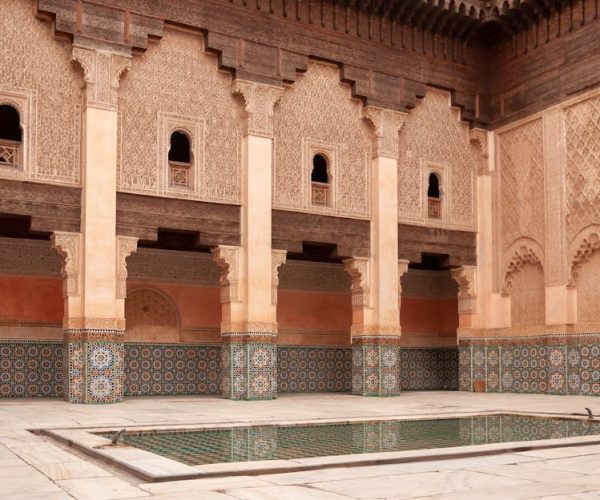 Main courtyard of ancient Ben Youssef Madrasa with arched passage and walls decorated with arabesque ornaments on sunny day in Marrakesh